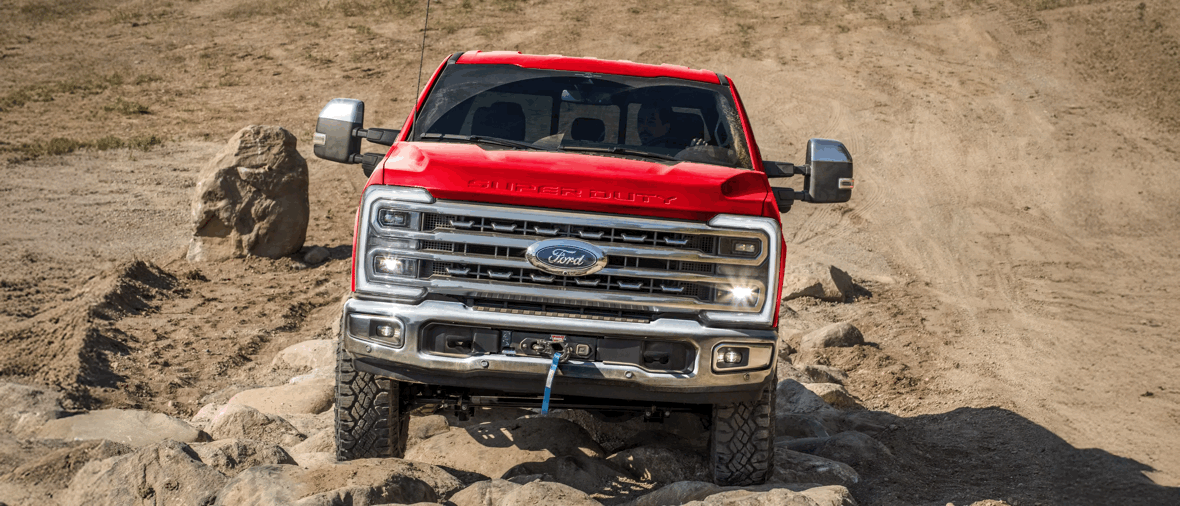 Ford Super Duty F-250 2026 rouge de face sur terrain rocheux, camion au design robuste avec éclairage amélioré.