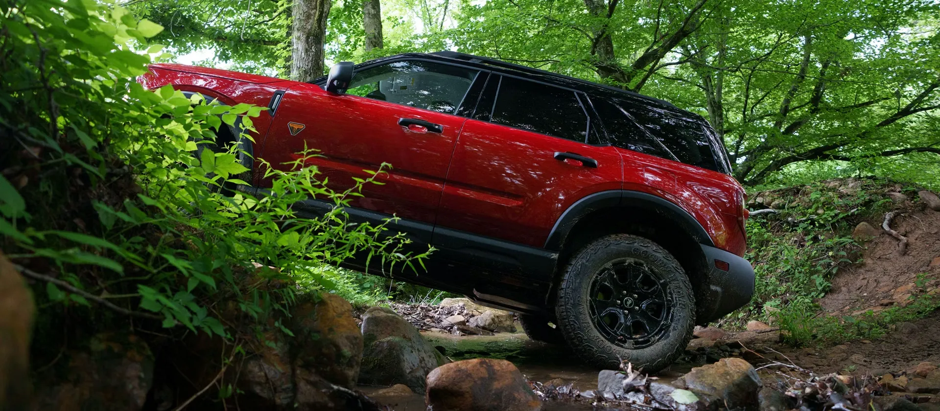 Ford Bronco Sport 2026 rouge franchissant un sentier rocheux en forêt.