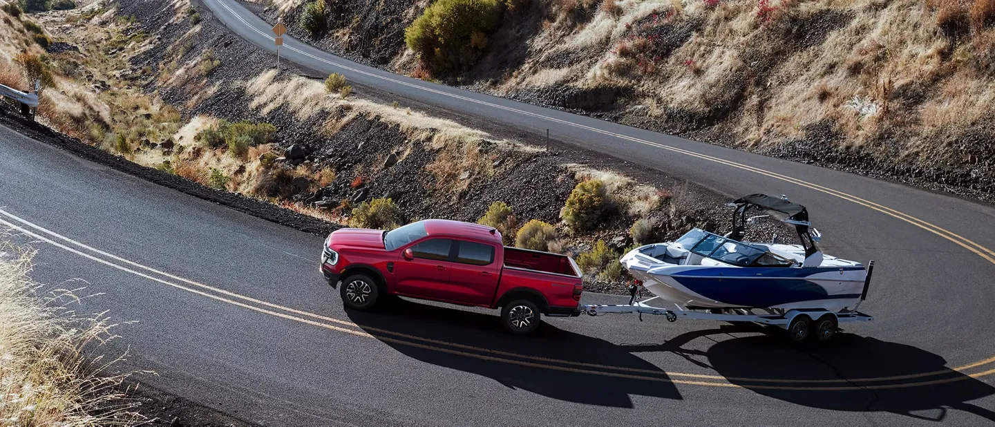 Ford Ranger 2026 rouge remorquant un bateau sur une route de montagne.