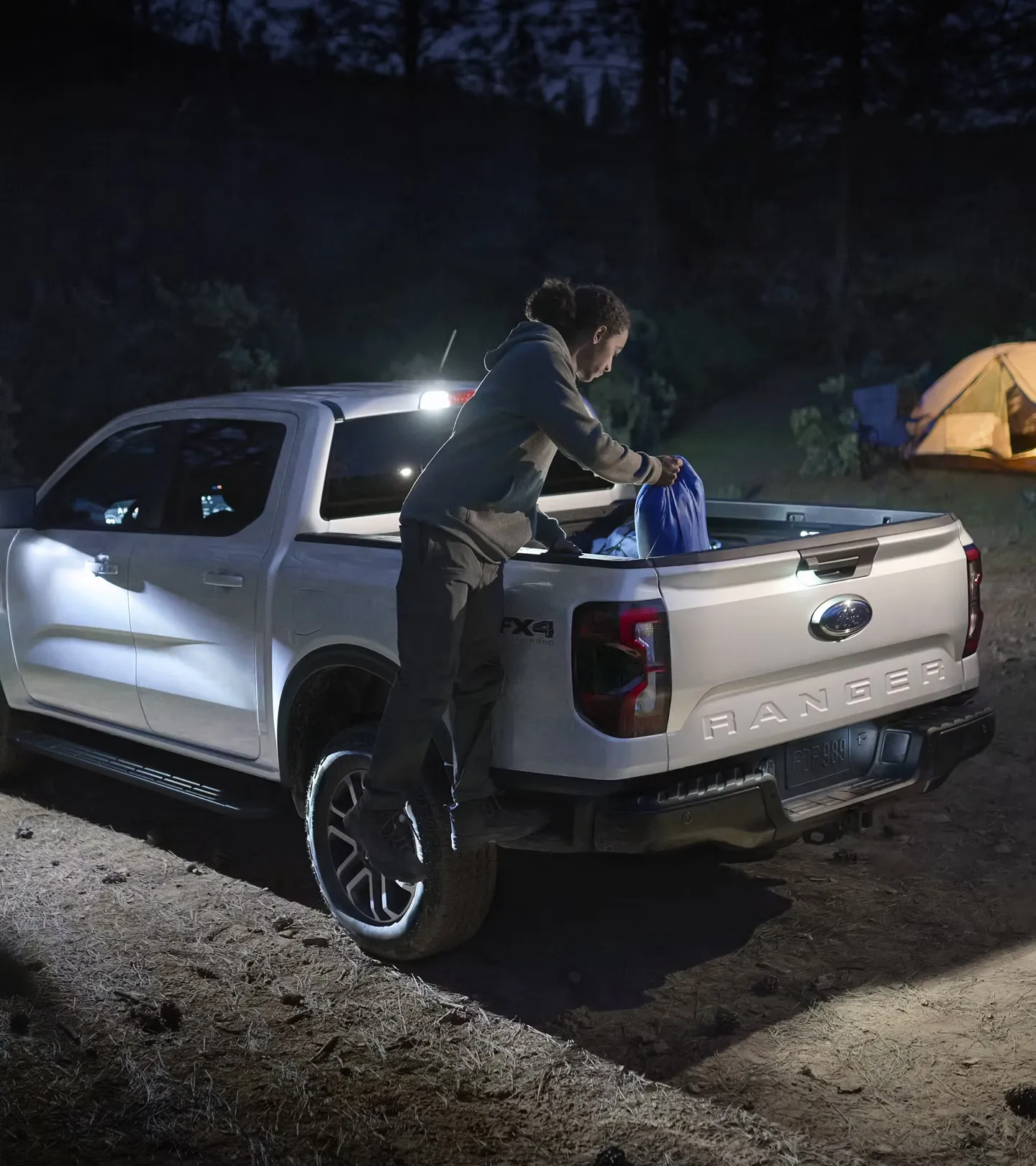 Chargement de matériel dans la caisse éclairée du Ford Ranger 2026 au camping.