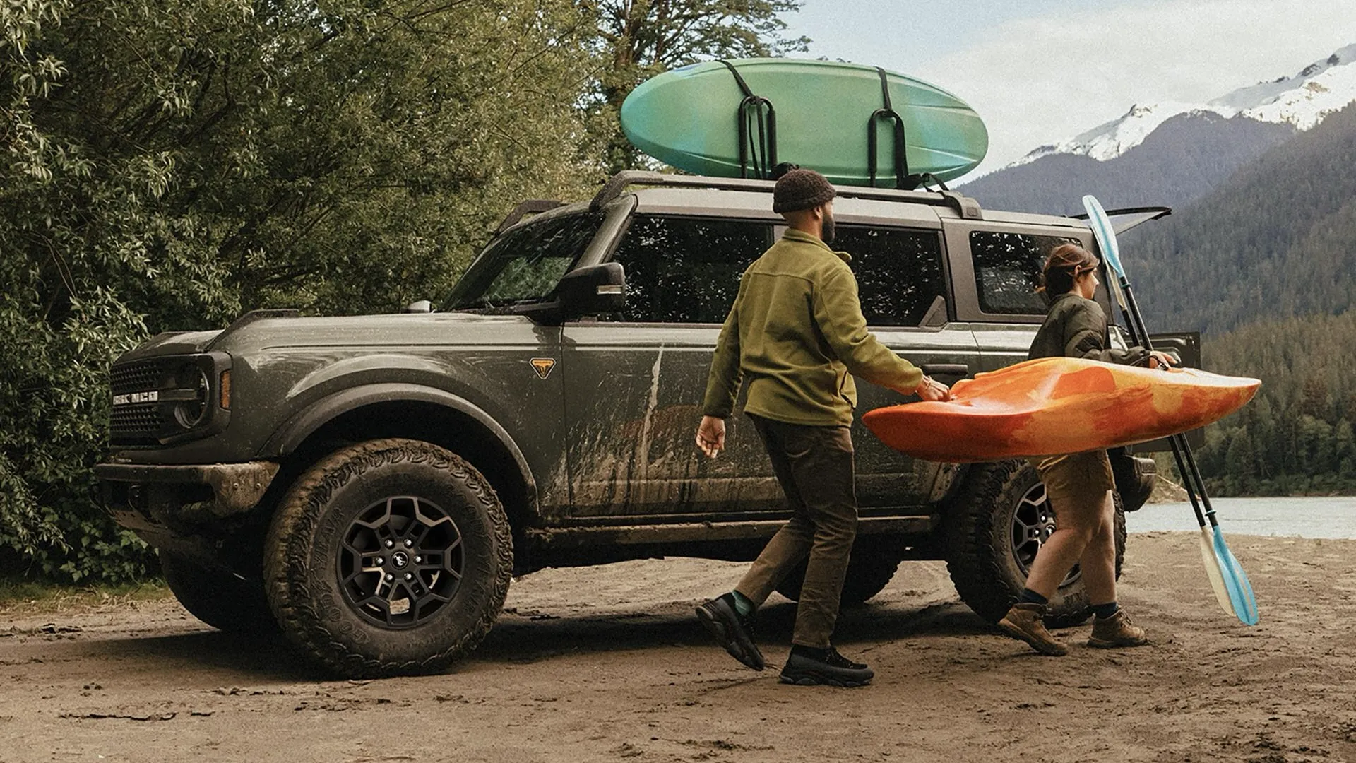 Ford Bronco 2026 au bord d'un lac, avec un kayak et des planches sur le toit pendant que deux personnes chargent leur équipement.