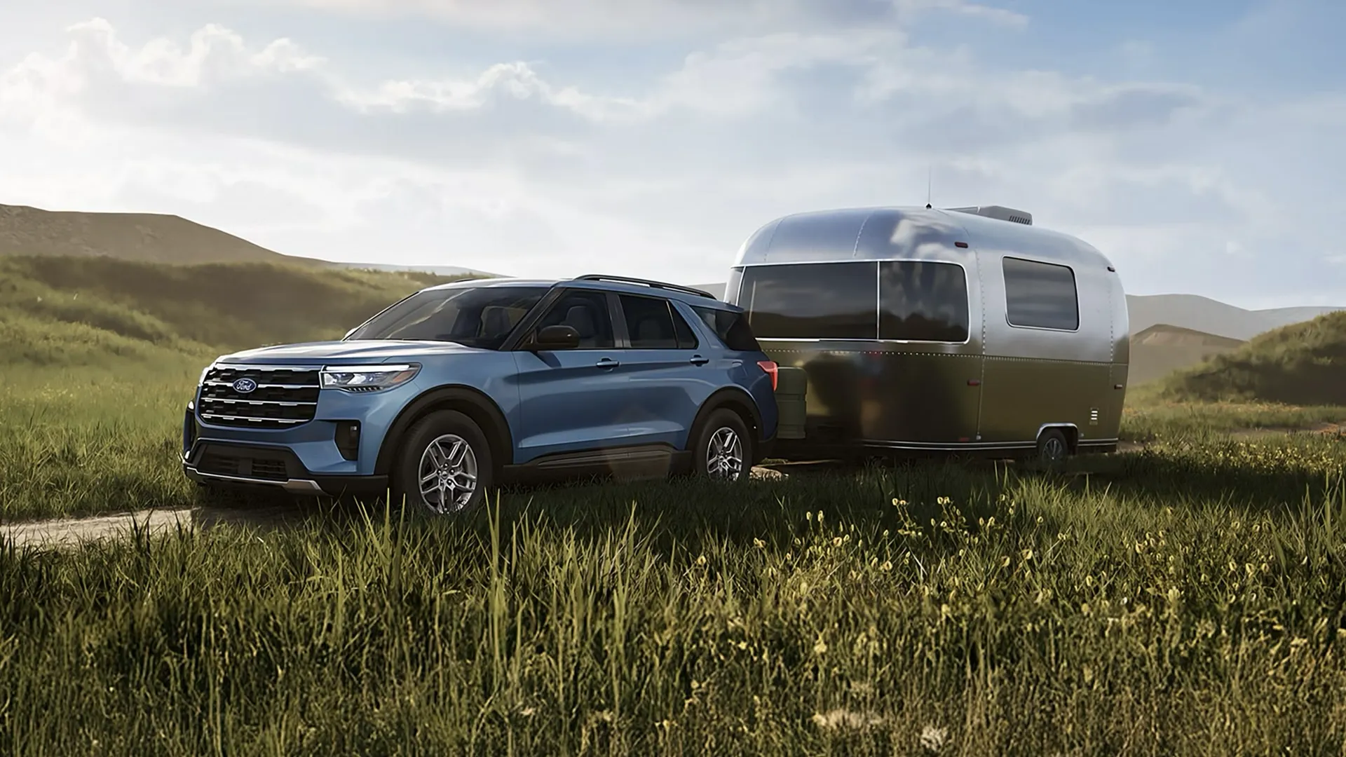 Ford Explorer 2027 bleu remorquant une roulotte argentée dans une vallée verdoyante.