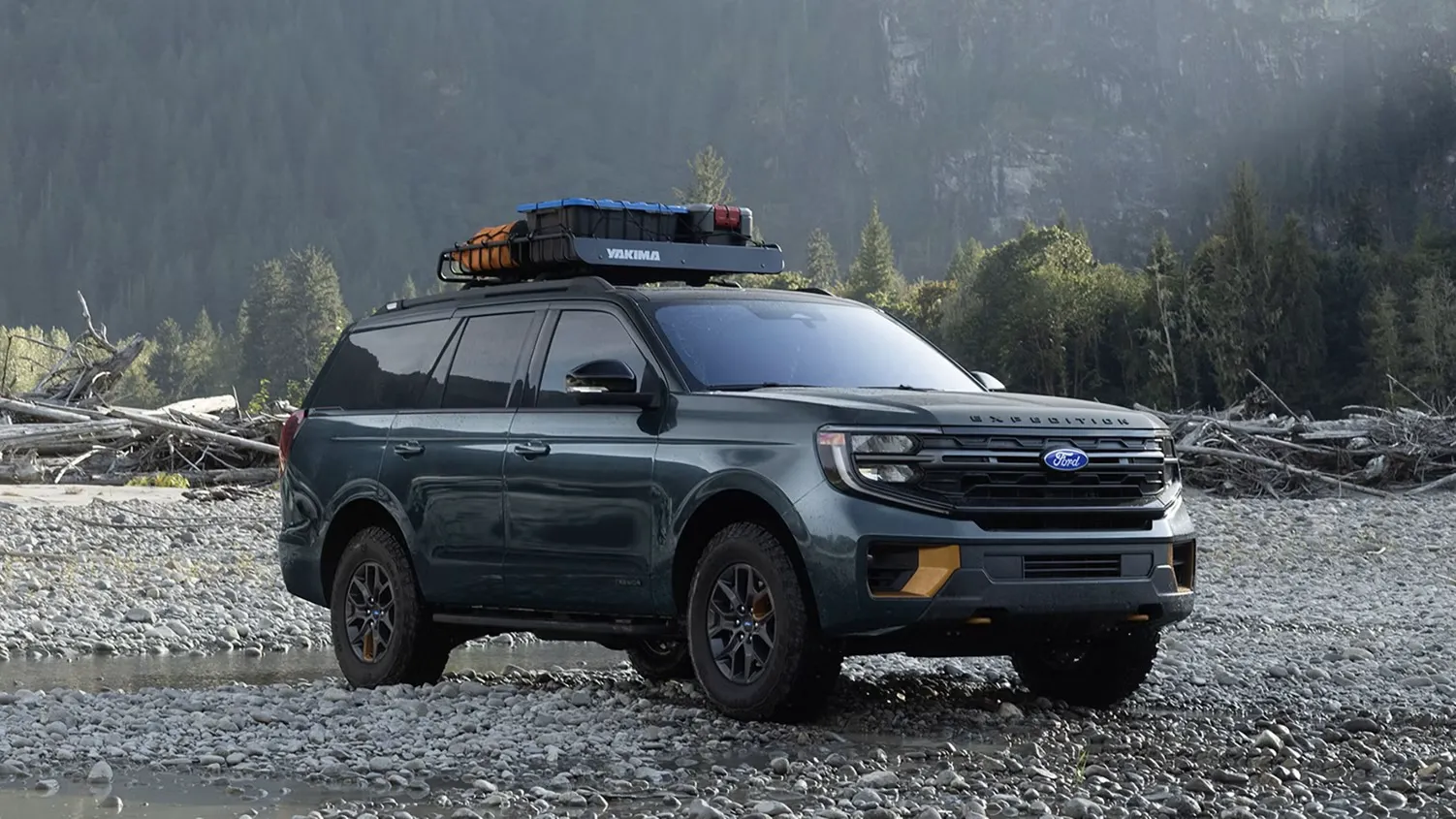 Ford Expedition 2027 gris foncé avec barres de toit, stationné sur un terrain de gravier devant des montagnes.