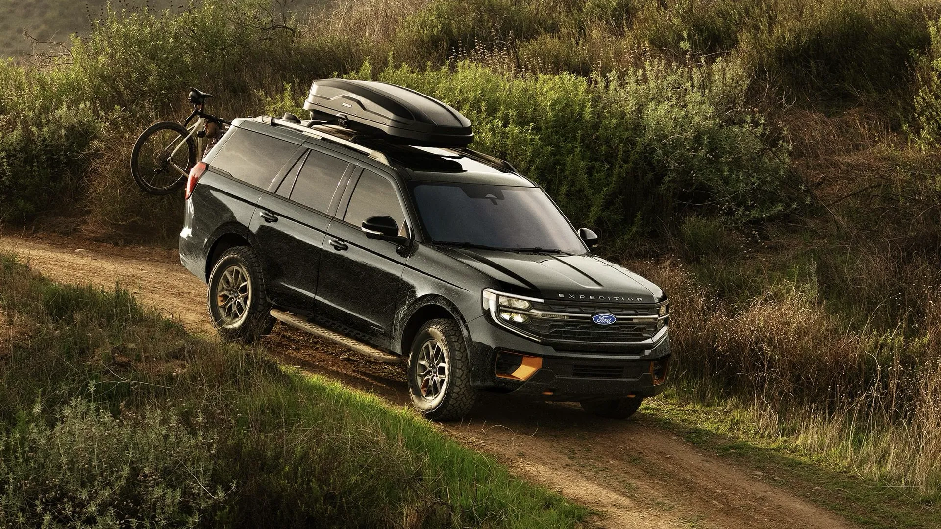 Ford Expedition 2026 avec bagages sur le toit, sur un chemin en forêt.