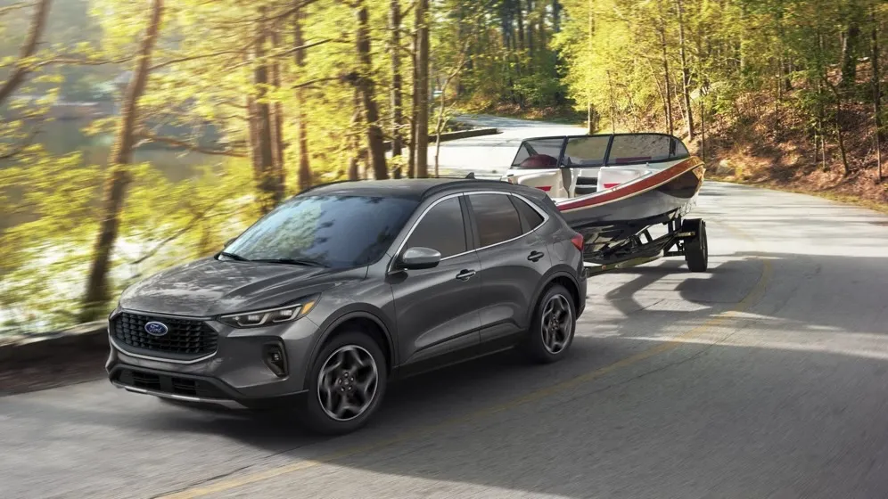 Ford Escape 2026 gris foncé remorquant un bateau sur une route en forêt à l'automne.