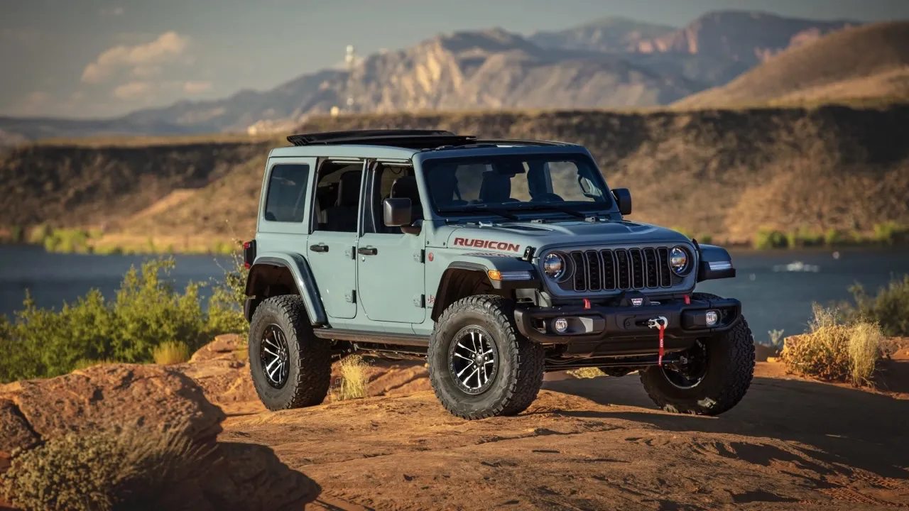 Jeep Wrangler 2026 gris bleuté stationné au bord d'un lac, devant des montagnes.