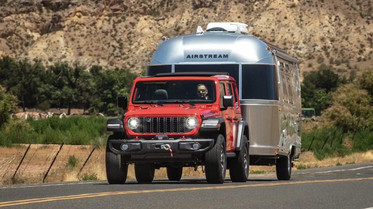 Jeep Wrangler 2026 rouge remorquant une roulotte argentée.
